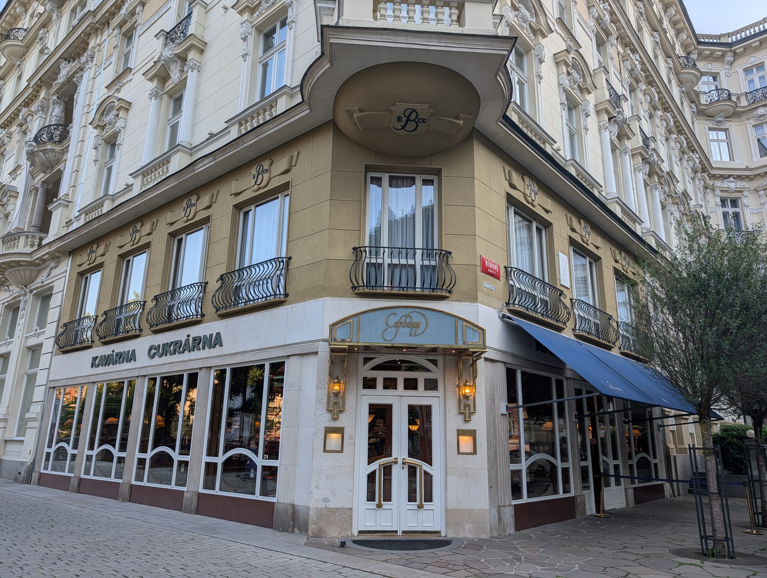 Eingang des Café Pupp in einem verzierten Eckgebäude mit Balkonen in Karlsbad