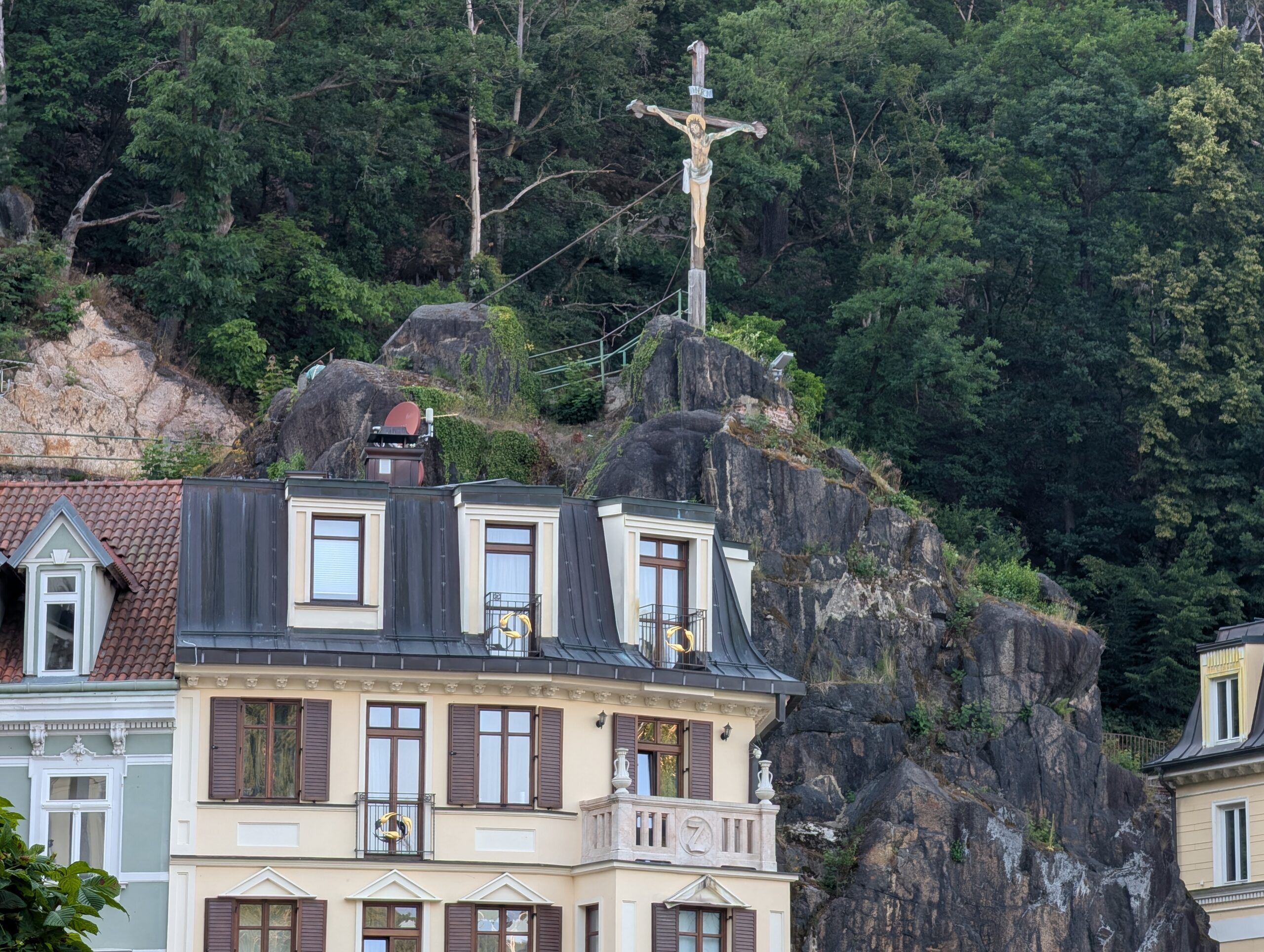 Keglewitsch-Kreuz auf einem bewaldeten Felsen über einem historischen Haus in Karlsbad