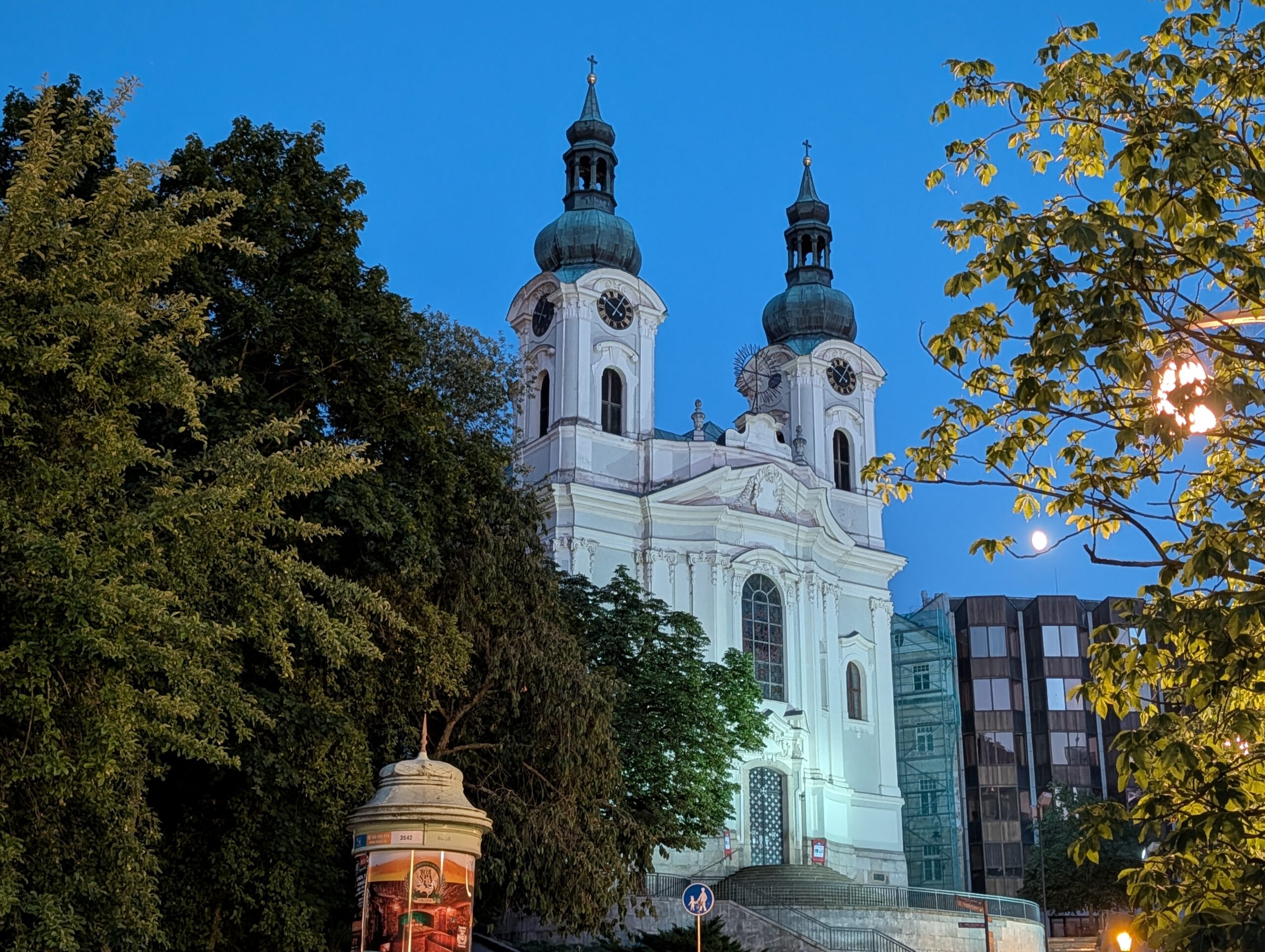 Beleuchtete Maria-Magdalenen-Kirche mit zwei Türmen zwischen Bäumen in Karlsbad