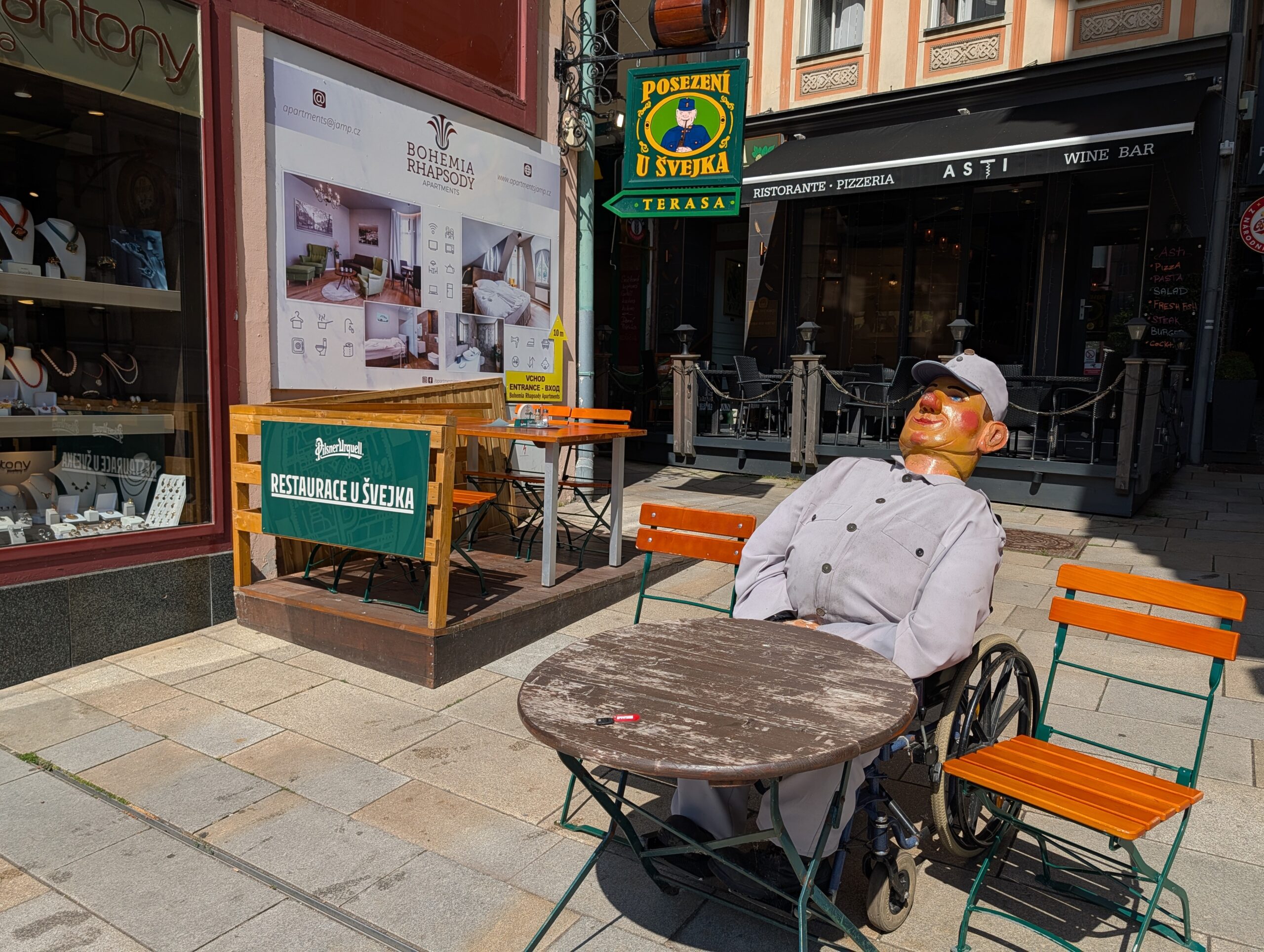 Schwejk-Figur im Rollstuhl an einem Tisch vor dem Restaurant U Švejka in Karlsbad.