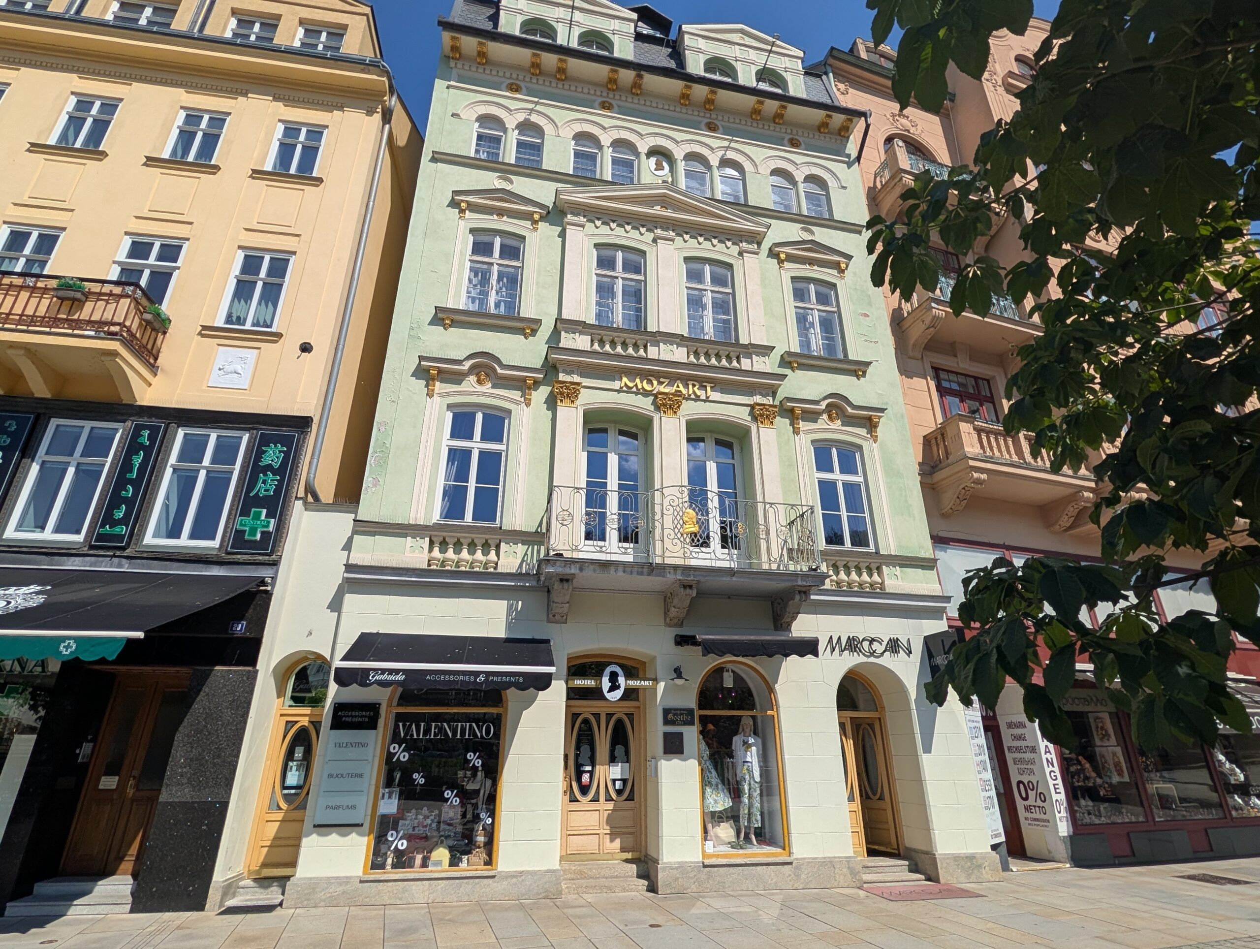 Hellgrüne Fassade des Mozart-Hauses in Karlsbad mit Balkon, verzierten Fenstern und Geschäften im Erdgeschoss.