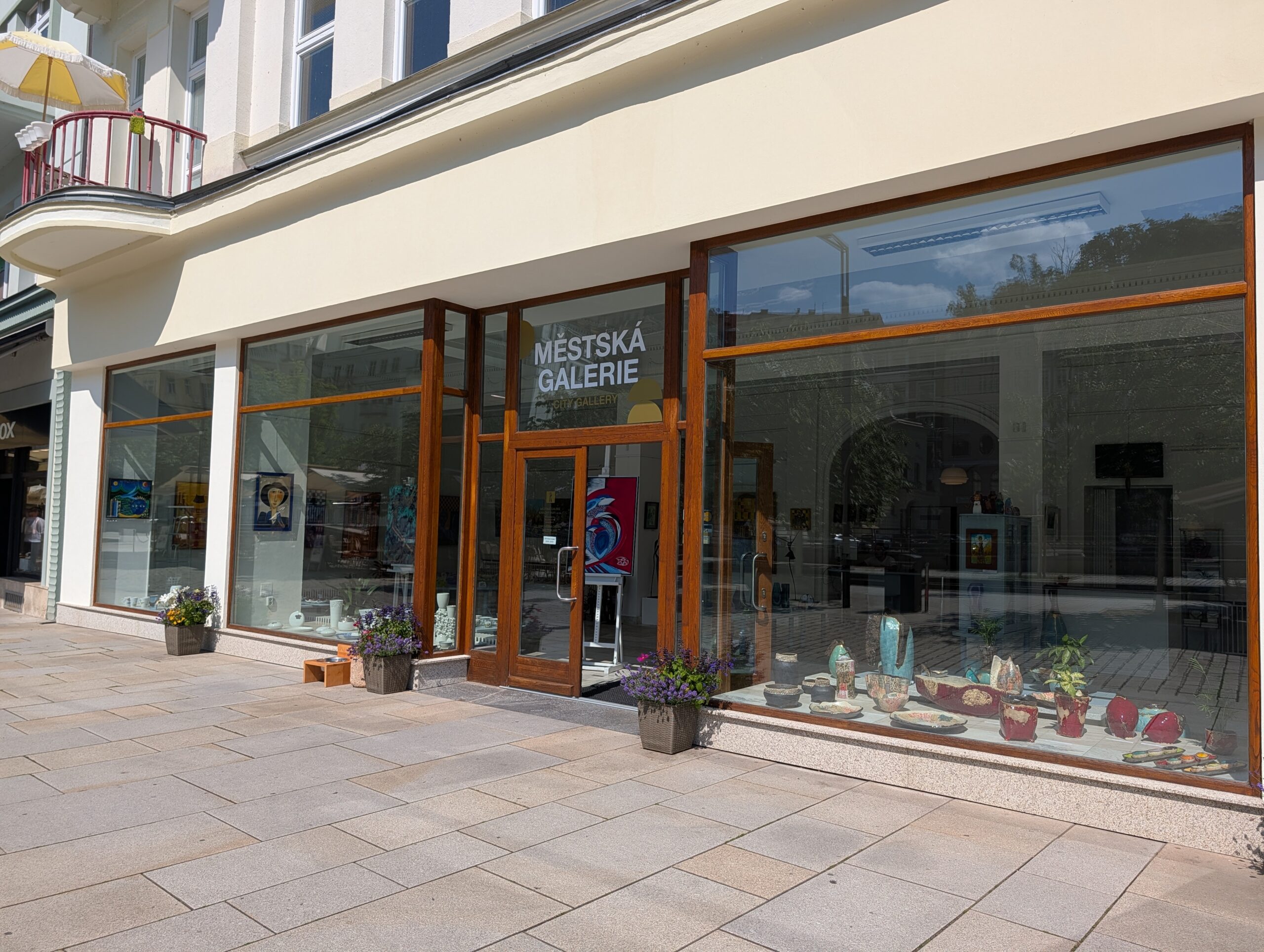 Städtische Galerie Karlsbad mit verglastem Eingang, großen Schaufenstern und ausgestellten Kunstobjekten.