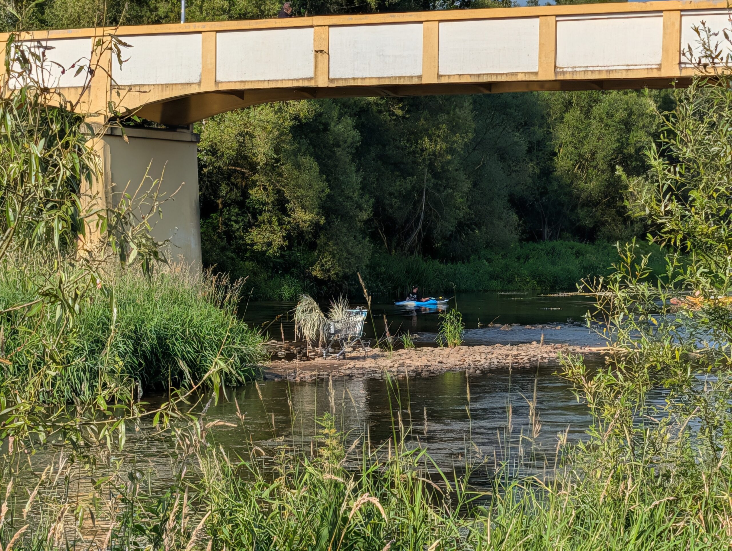 Brücke über die Eger mit Blick auf die Enteninsel (Kachní ostrov), Kanufahrer und naturbelassenes Flussufer in Karlsbad.