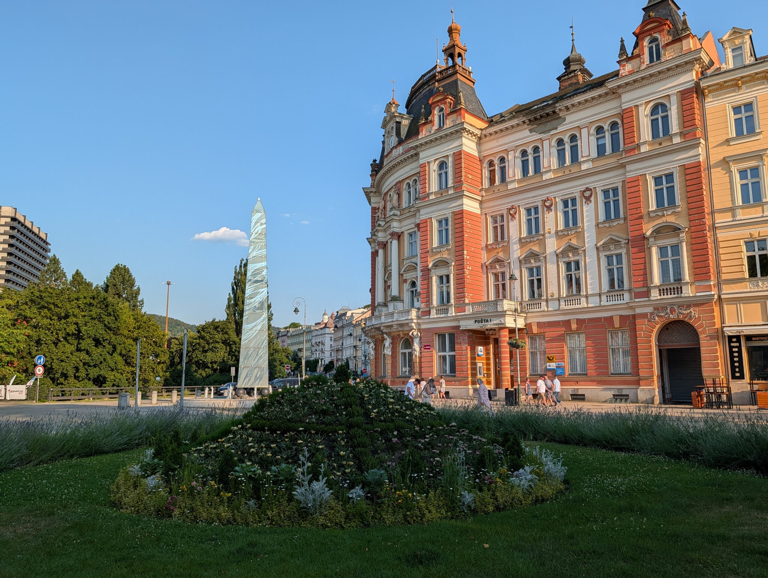 Glasobelisk auf einem bepflanzten Brunnen vor historischen Gebäuden am T.-G.-Masaryk-Platz in Karlsbad.