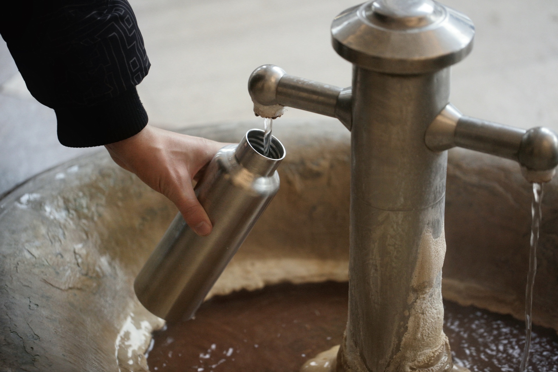 Person füllt Karlsbader Thermalwasser an einem Quellbrunnen in eine Edelstahlflasche