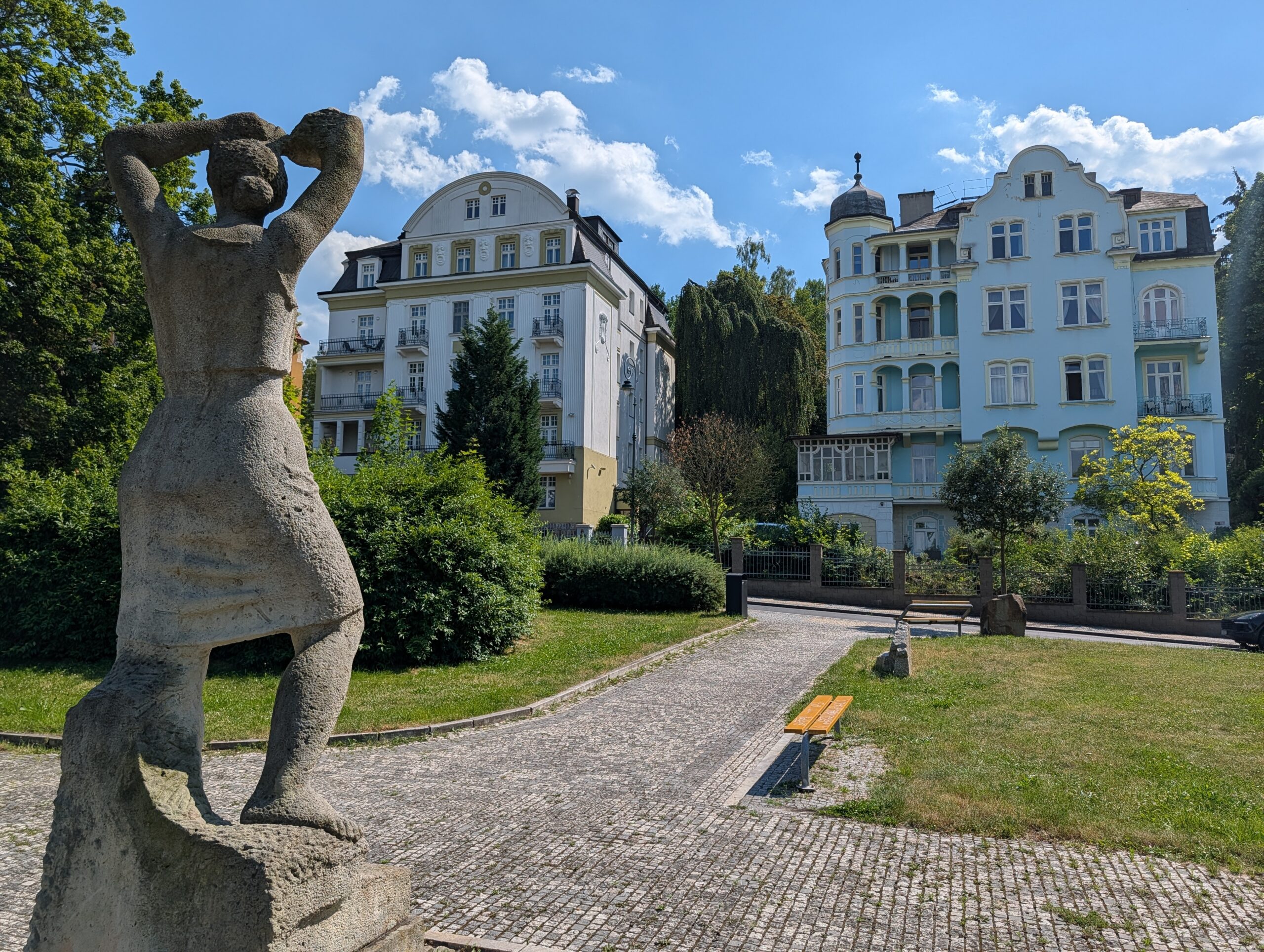Steinerne Frauenfigur in einer Parkanlage vor historischen Wohnhäusern.